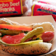 Hot dog with everything in a paper boat beside packs of Vienna Beef hot dogs